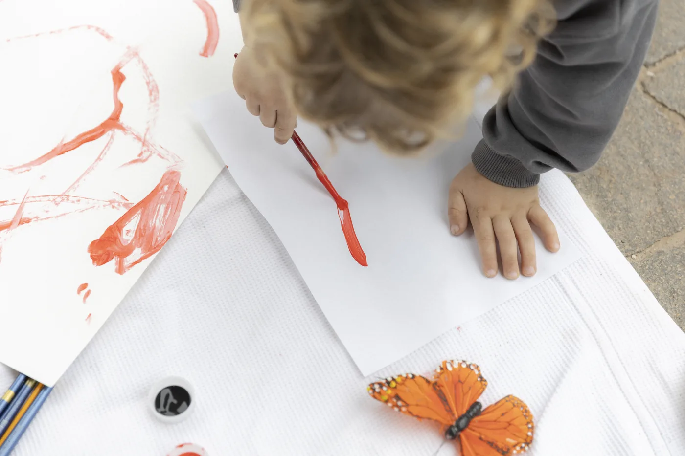 Un niño pinta con témpera roja junto a una mariposa de papel