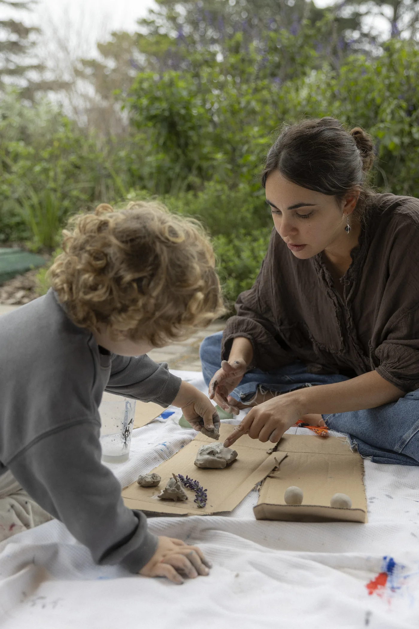 Una niña y una adulta trabajan con arcilla y materiales naturales al aire libre